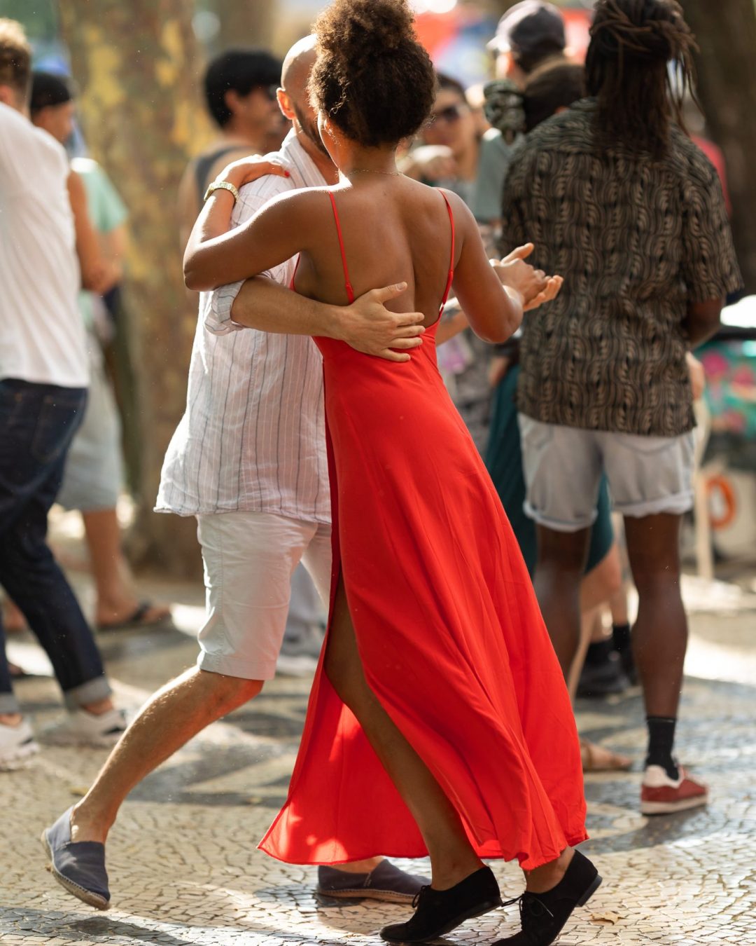 Couples dancing on the street - tanned woman wearing red bright dress in the centre. Mid shot